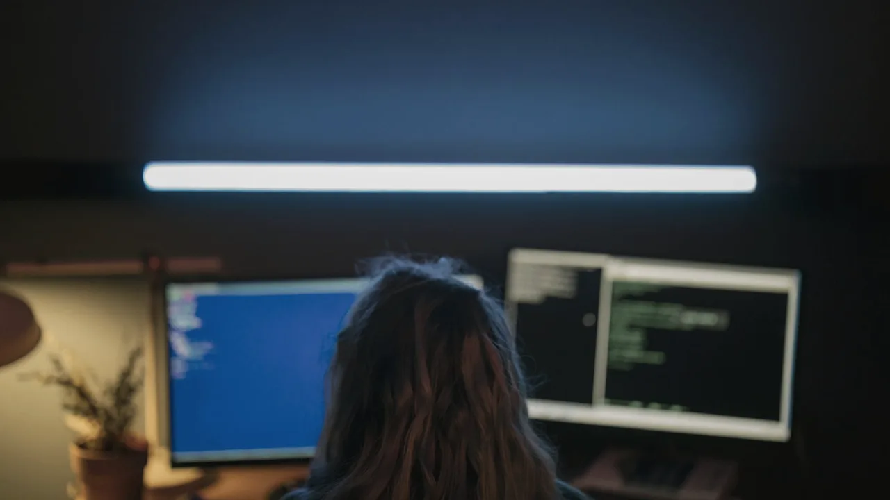 Pessoa em frente ao computador em ambiente de trabalho com luz baixa