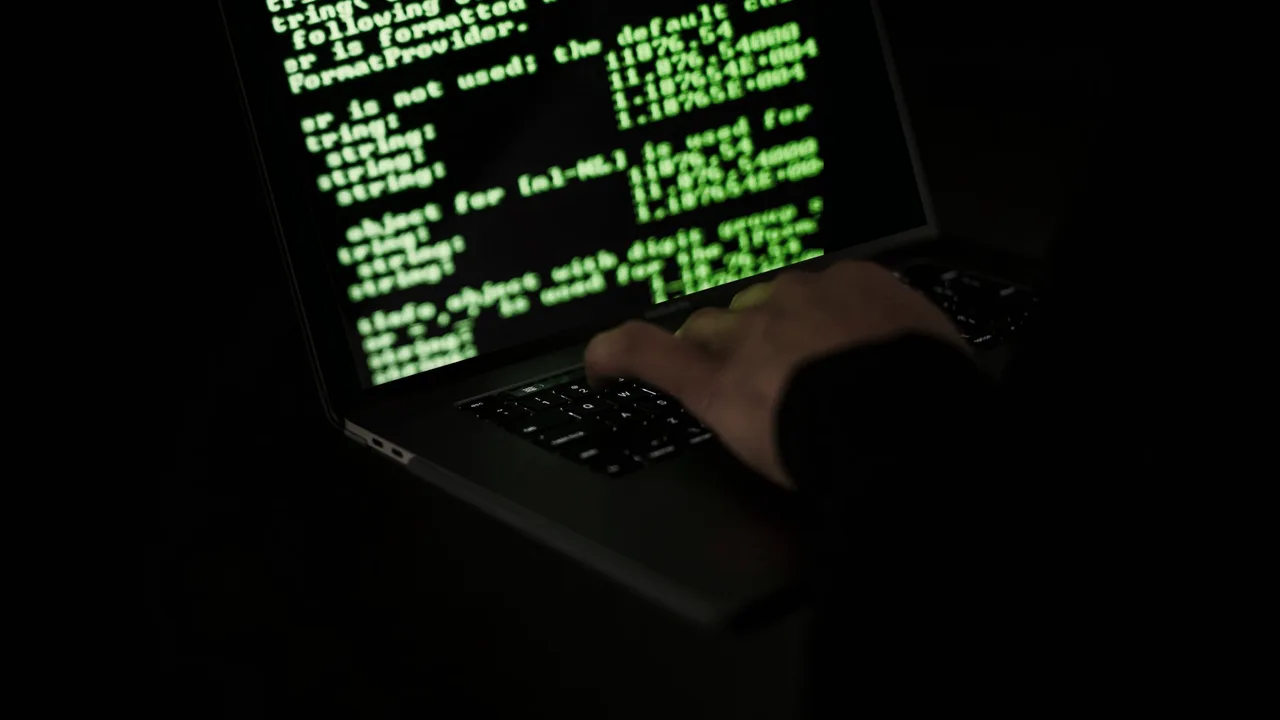 Mão sobre o teclado de um notebook com uma tela de código em verde, em ambiente escuro