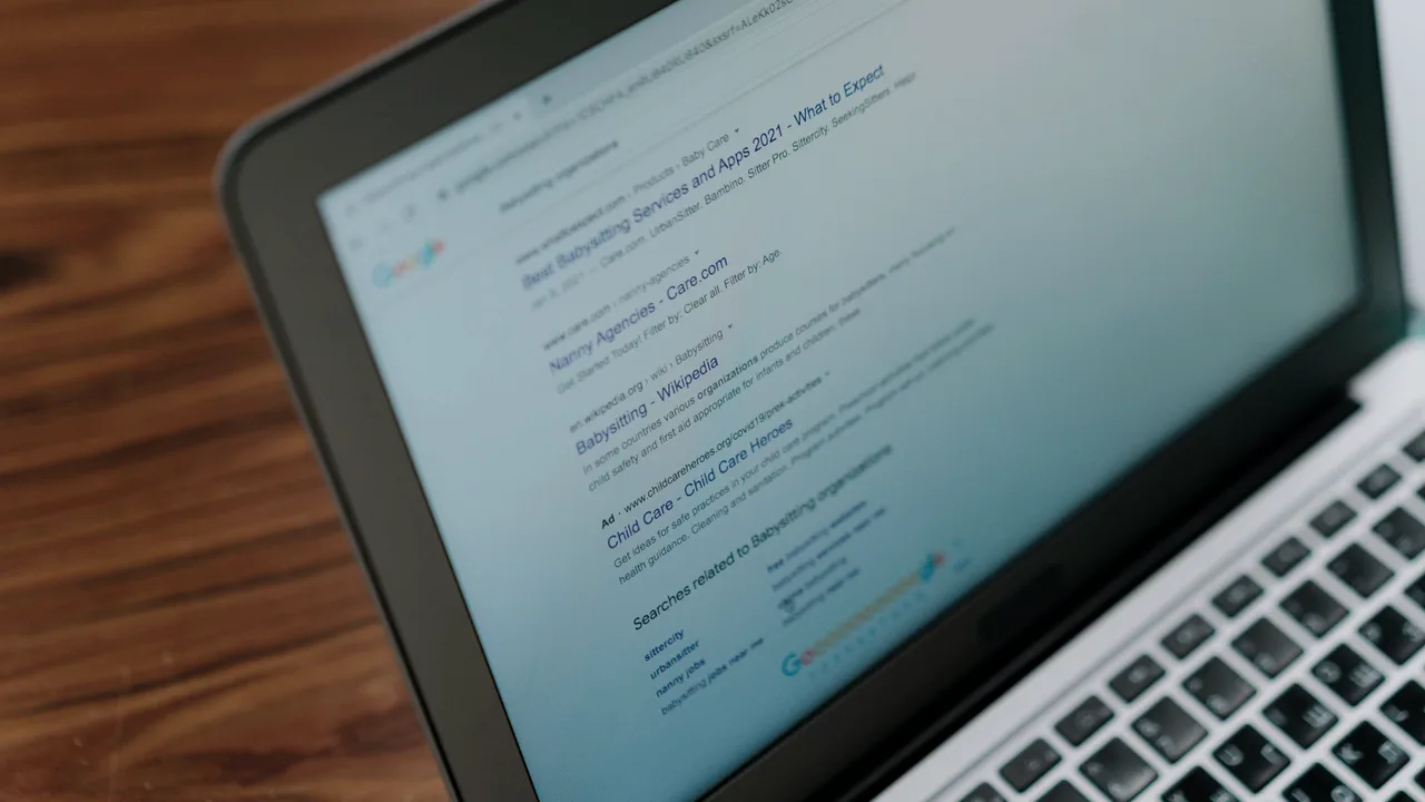 Tela de notebook mostrando uma página de resultados do Google, com links orgânicos, um anúncio e o bloco de buscas relacionadas, sobre mesa de madeira