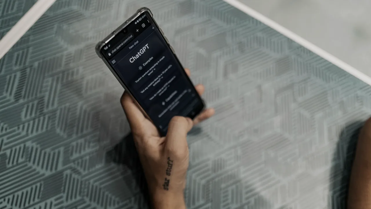 Mão segurando um celular com a tela do ChatGPT aberta, pronta pra fazer uma pergunta