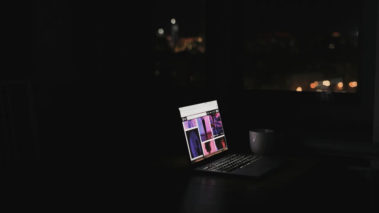 Notebook aceso numa sala escura à noite, com as luzes da cidade ao fundo pela janela