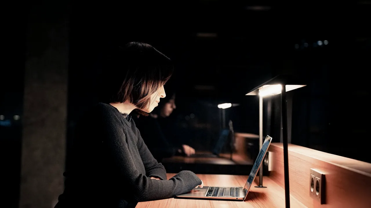 Pessoa concentrada no notebook à noite, com luz baixa na mesa