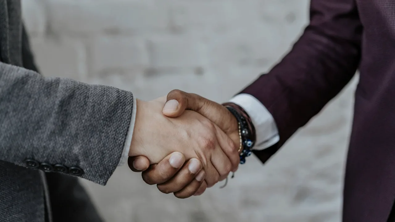 aperto de mão em close entre duas pessoas de terno, simbolizando uma conexão real entre duas partes