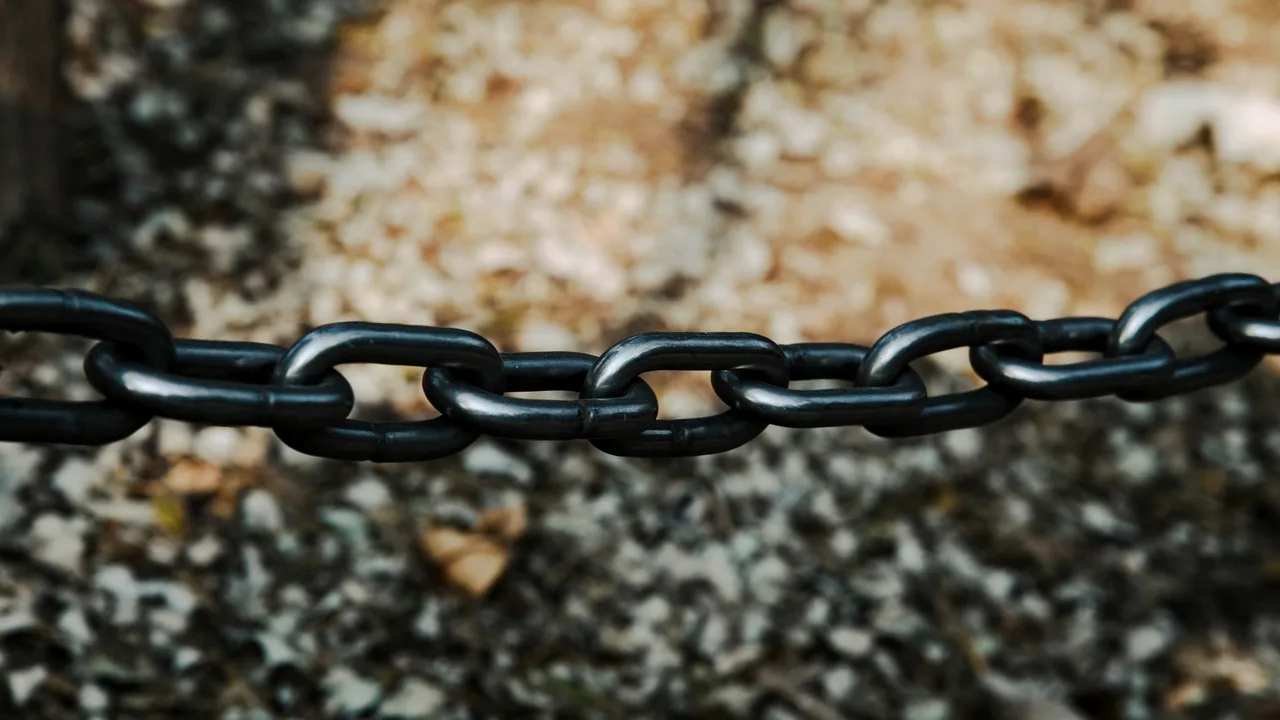 corrente de metal escura com elos entrelaçados, em close, contra fundo desfocado