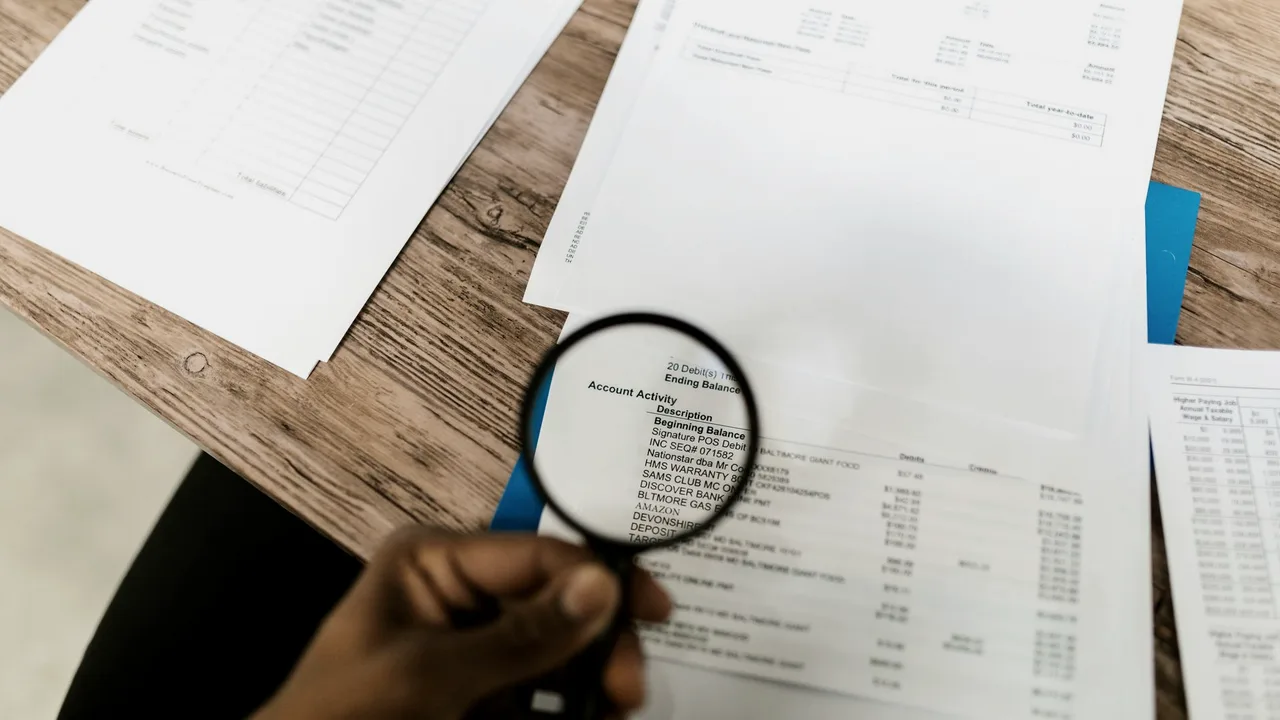 Mão usando lupa para examinar de perto um documento sobre uma mesa