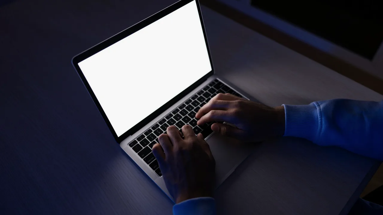 Pessoa trabalhando tarde da noite num notebook com a tela em branco, iluminada pela luz da própria tela