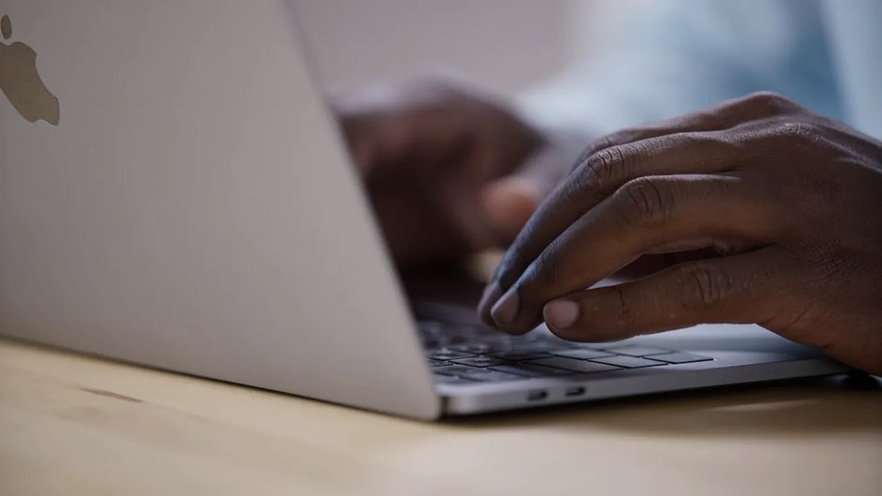 Close-up de mãos digitando no teclado de um notebook, em ambiente com pouca luz