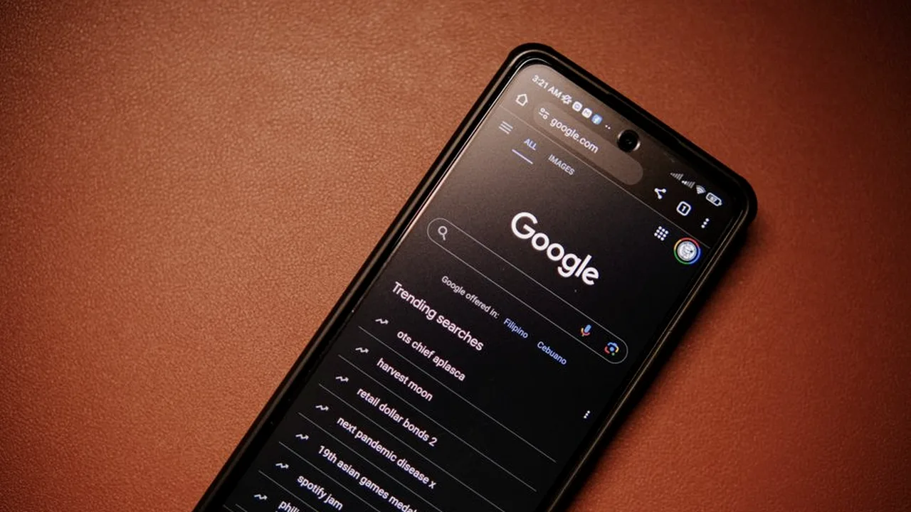 Celular na mão mostrando a tela de busca do Google aberta, em ambiente escuro com luz quente