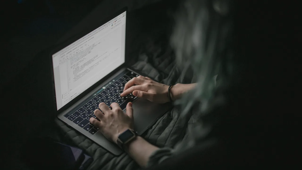Mãos digitando num notebook à noite, com código aberto na tela