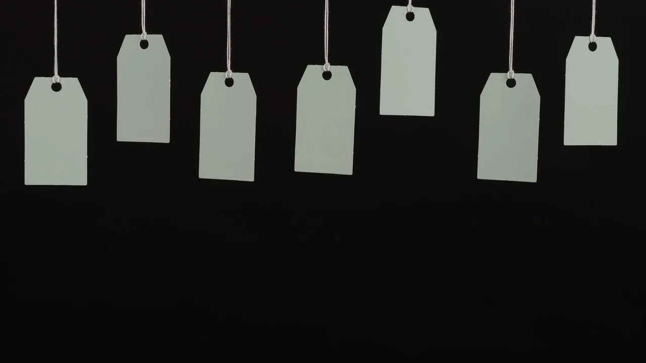 Etiquetas de preço em branco, sem nenhum valor escrito, penduradas contra um fundo preto