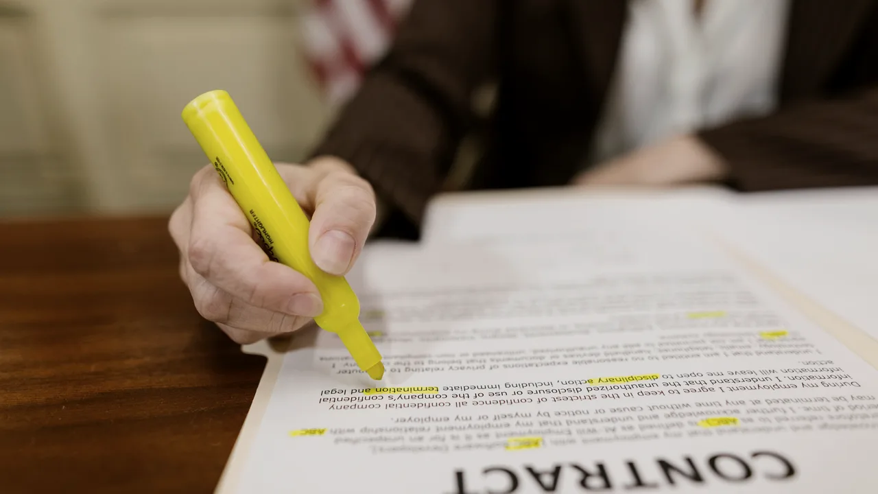 mão segurando um marca-texto amarelo e grifando trechos de um documento impresso sobre uma mesa de madeira escura