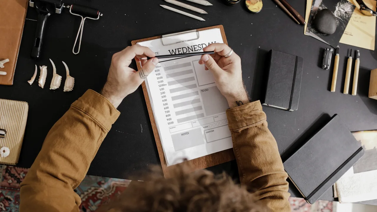 Pessoa preenchendo um planner semanal com os horários do dia, numa mesa de trabalho