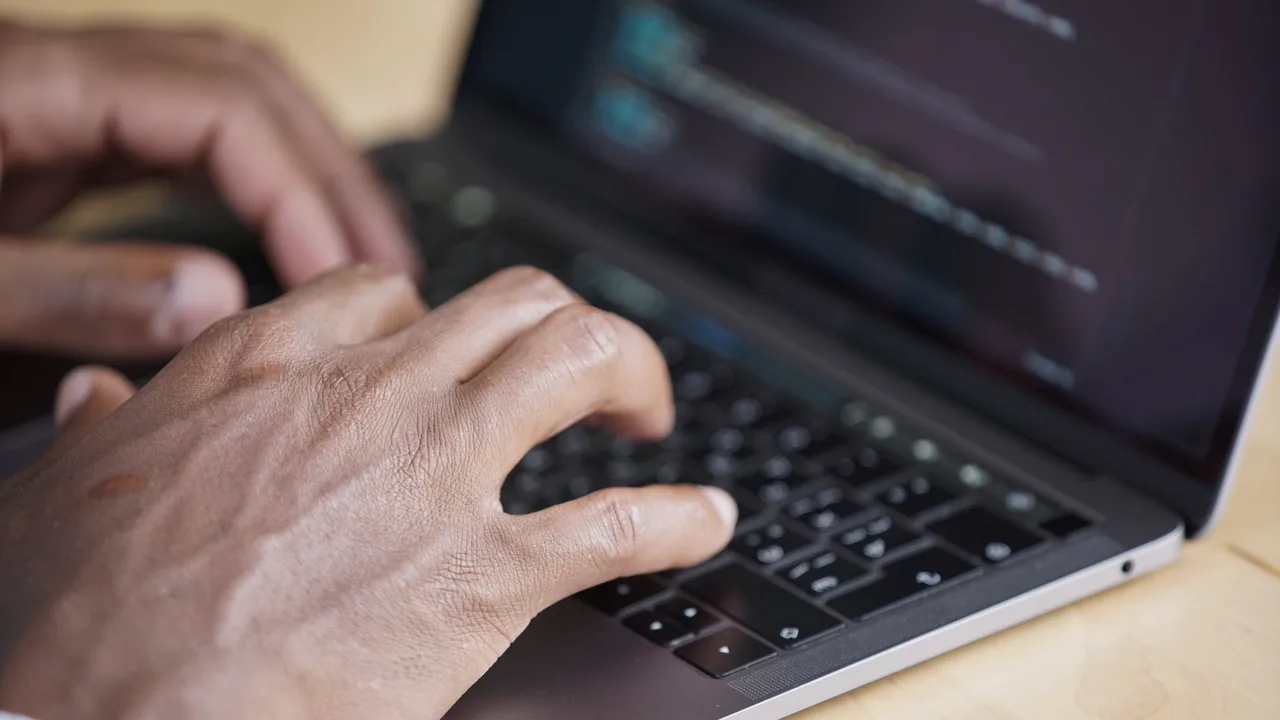 Mãos digitando em um laptop escuro com linhas de código visíveis na tela