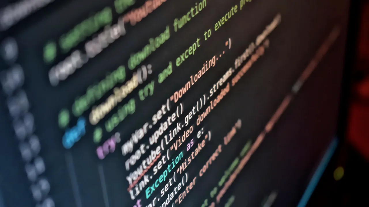 Tela de computador em ambiente escuro mostrando linhas de código coloridas e desfocadas