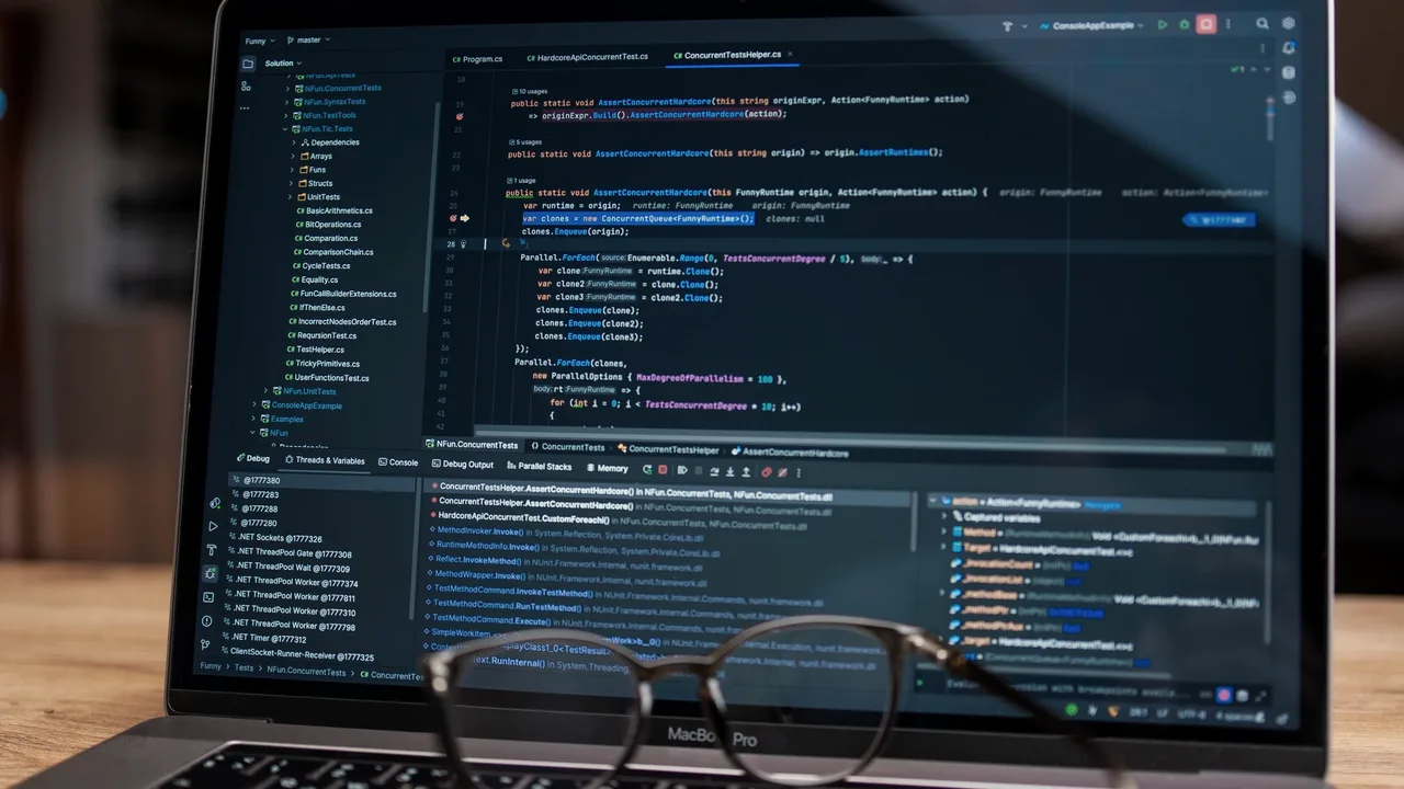Tela de laptop mostrando código de programação em ambiente escuro, com óculos apoiados na frente